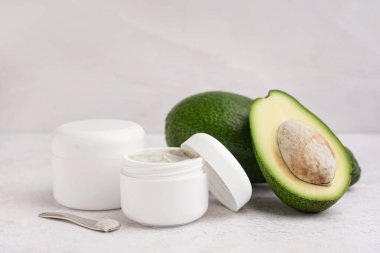 Hafif arka planda taze avokado ve kozmetik ürünleri kavanozları, yakın plan