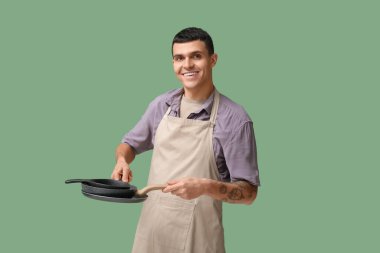 Yeşil arka planda kızartma tavaları olan yakışıklı genç adamın portresi.