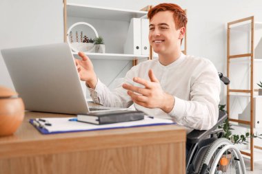 Tekerlekli sandalyedeki genç işadamı ofiste video sohbeti yapıyor.