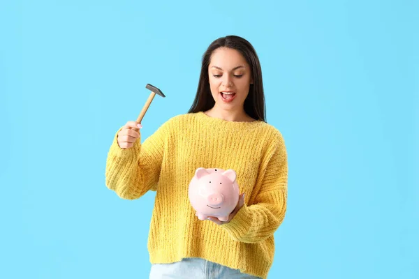 Young woman with hammer and piggy bank on blue background