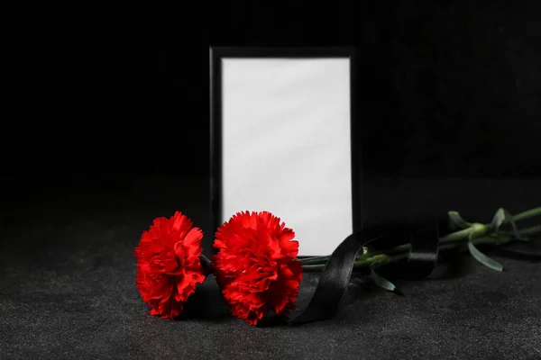 Blank funeral frame with black ribbon and carnation flowers on dark background