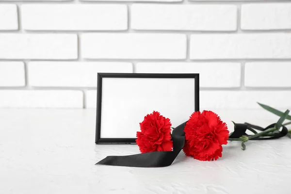 Blank funeral frame, carnation flowers and blank ribbon on table near light brick wall