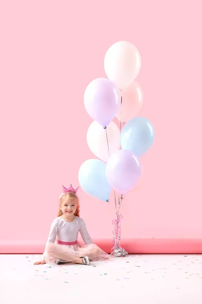 Cute little girl with beautiful balloons sitting on pink background