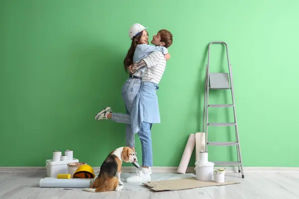 Young couple with Beagle dog hugging near green wall during repair in their new house