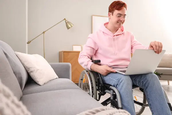 Young man in wheelchair with laptop at home