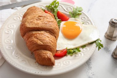 Hafif arka planda lezzetli yumurta, kruvasan, domates ve roka tabağı, yakın plan.