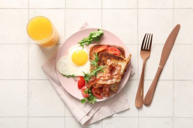 Lezzetli sahanda yumurta, tost, pastırma, domates ve arka planda bir bardak meyve suyu.