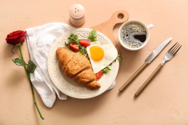 Lezzetli kızarmış yumurta, kruvasan, domates, bir fincan kahve ve bej arka planda gül çiçeği karışımı.