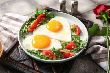 Lezzetli sahanda yumurta, domates, roka ve gül çiçekli gri kaplama, yakın plan.