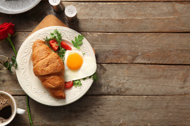 Lezzetli kızarmış yumurta, kruvasan, bir fincan kahve ve ahşap zemin üzerinde gül çiçeği.