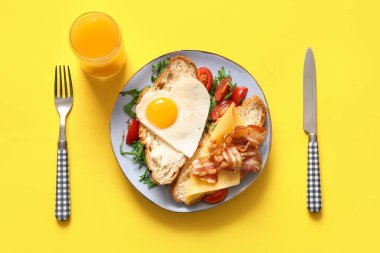 Lezzetli kızarmış yumurta, kruvasan, pastırma, domates ve sarı arka planda bir bardak meyve suyu.