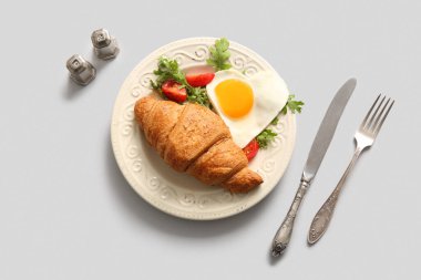 Beyaz arka planda lezzetli yumurta, kruvasan, domates ve roka tabağı.