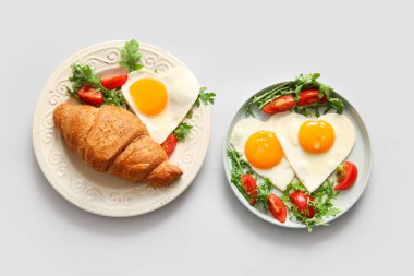 Beyaz arka planda lezzetli kızarmış yumurta, kruvasan, domates ve roka tabakları.