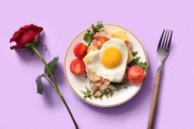 Lezzetli kızarmış yumurta, pastırma, tabakta domates, mor arka planda gül çiçeği ve çatal.