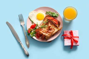 Lezzetli kızarmış yumurta, tost, domates, roka, bir bardak meyve suyu ve mavi arka planda hediye paketi.