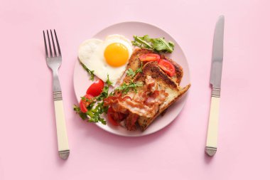 Lezzetli kızarmış yumurta, tost, domates, roka ve pembe arka planda çatal bıçak takımı.
