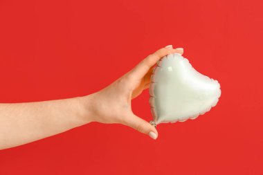 Kırmızı arka planda kalp şeklinde hava balonu olan bir kadın eli. Sevgililer Günü kutlaması