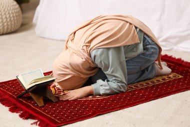 Kuran ile tesettürlü küçük Müslüman kız evde dua ediyor.