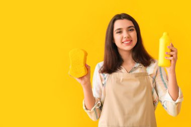 Sarı arka planda sünger ve bir şişe deterjanı olan genç bir kadın.