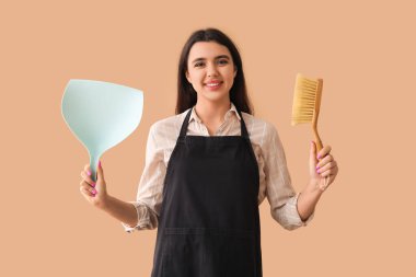 Bej arka planda faraş ve fırçayla genç bir kadın.