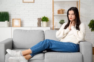 Tiroid bezi sorunu olan genç bir kadın evdeki kanepede oturuyor.