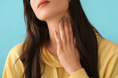 Mavi arka planda tiroit bezi sorunu olan genç bir kadın, yakın plan.