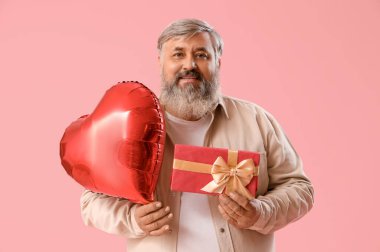 Kalp şeklinde balonu ve pembe arka planda hediye kutusu olan mutlu olgun bir adam. Sevgililer Günü kutlaması