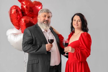 Kalp şeklinde balonları ve gri arka planda şarap bardakları olan güzel, olgun bir çift. Sevgililer Günü kutlaması