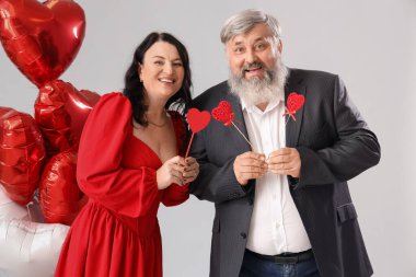 Gri arka planda kalp şeklinde balonları ve kalpleri olan güzel olgun bir çift. Sevgililer Günü kutlaması