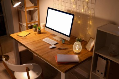 Boş bilgisayar monitörlü işyeri, geceleri ofiste parlayan ışıklar ve pano.