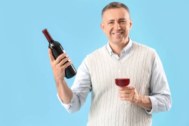 Yakışıklı, olgun bir adam, mavi arka planda bir şişe ve bir bardak şarap.