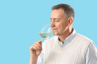 Mavi arka planda şarap kadehi olan yakışıklı olgun bir adam.