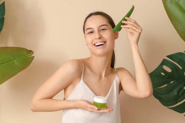 Bitki yaprakları ve bej arka planda bir kavanoz aloe vera jeli güzel, mutlu bir kadın.