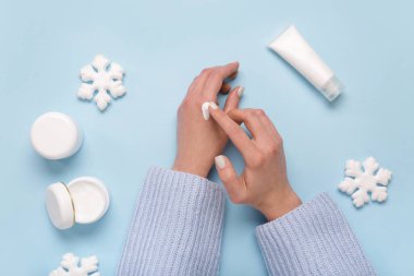 Kozmetik ürünleri ve mavi arka planda dekoratif kar taneleri olan kadın elleri