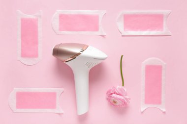 Balmumu şeritli modern fotoepilatör ve pembe arka planda çiçek.