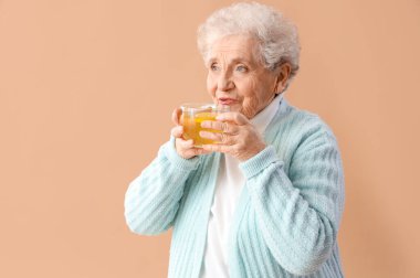 Bej arka planda cam bardak sıcak limon çayı olan olgun bir kadın.