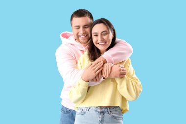 Mutlu genç çift mavi arka planda sarılıyor