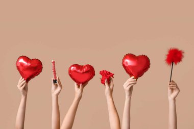 Kalp şeklinde balonları ve bej arka planda seks oyuncakları olan birçok kadın eli. Sevgililer Günü kutlaması