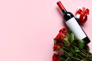 Güllü bir şişe şarap ve pembe arka planda bir hediye. Sevgililer Günü kutlaması