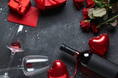 Kırmızı güllerden, gözlüklerden, bir şişe şaraptan, hediye kutularından ve siyah arka planda kalp şeklinde balonlardan yapılmış çerçeveler. Sevgililer Günü kutlaması