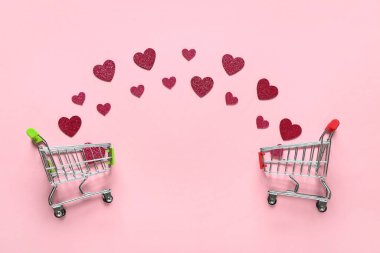 Pembe arka planda kağıt kalpli küçük alışveriş arabaları. Sevgililer Günü kutlaması