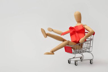 Tahta heykelciği ve beyaz arka planda hediye kutusu olan küçük bir alışveriş arabası. Sevgililer Günü kutlaması
