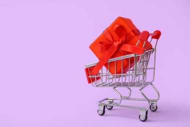 Leylak arka planında hediye kutusu olan küçük bir alışveriş arabası. Sevgililer Günü kutlaması