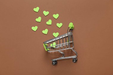 Kahverengi arka planda kalpleri olan küçük bir alışveriş arabası. Sevgililer Günü kutlaması