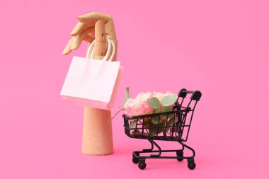Çiçekli küçük alışveriş arabası, ahşap el ve pembe arka planda kağıt torba. Sevgililer Günü kutlaması