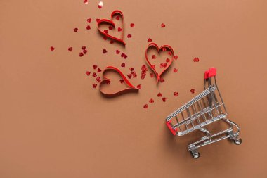 Kahverengi arka planda kalpleri olan küçük bir alışveriş arabası. Sevgililer Günü kutlaması