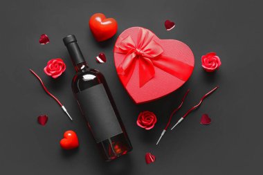 Bir şişe şarap, hediye kutusu ve siyah arka planda dekor. Sevgililer Günü kutlaması