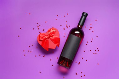 Hediye kutulu bir şişe şarap ve mor arka planda konfeti. Sevgililer Günü kutlaması