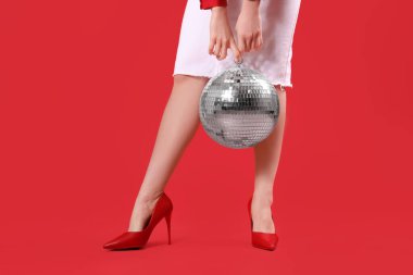 Kırmızı arka planda disko topu olan güzel genç bayanın bacakları, yakın plan.