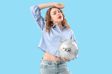 Mavi arka planda disko topu olan güzel, genç ve şık bir kadın.